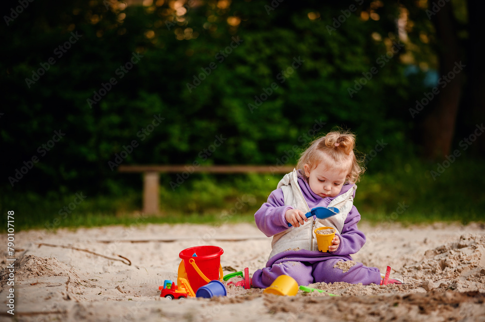 Engrossed in play, a young toddler fills a cup with sand, surrounded by colorful toys in a sandbox, a picture of focus and discovery Engrossed in play, a young toddler fills a cup with sand, surrounded by colorful toys in a sandbox, a picture of focus and discovery