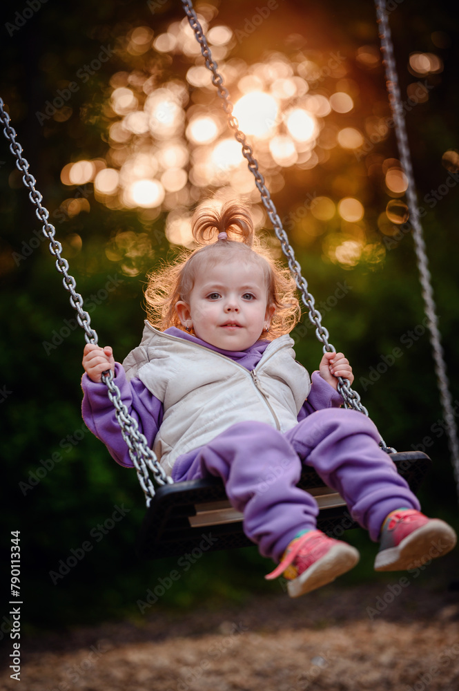 A young child gazes into the distance while swinging alone, surrounded by the tranquil light of the setting sun filtering through the trees A young child gazes into the distance while swinging alone, surrounded by the tranquil light of the setting sun filtering through the trees