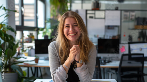 Surrounded by sleek office dÃ©cor and modern furnishings, a beautiful white woman clasps her hands together in delight, her computer screen displaying positive results, her beaming