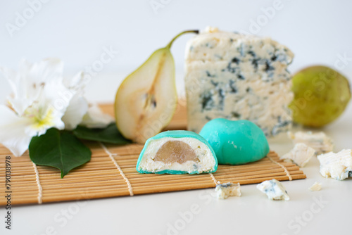 Mochi green color on bamboo makisu with flowers, pear and blue cheese on light background. Japanese traditional frozen delicious dessert mochi. ice cream with dough of sticky rice. Asian cuisine.