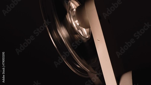 close up of a film projector reel spool turning with a super 8 mm film strip running shaking changing frames detail shot isolated on black background side view old equipment cinematography 4K HQ