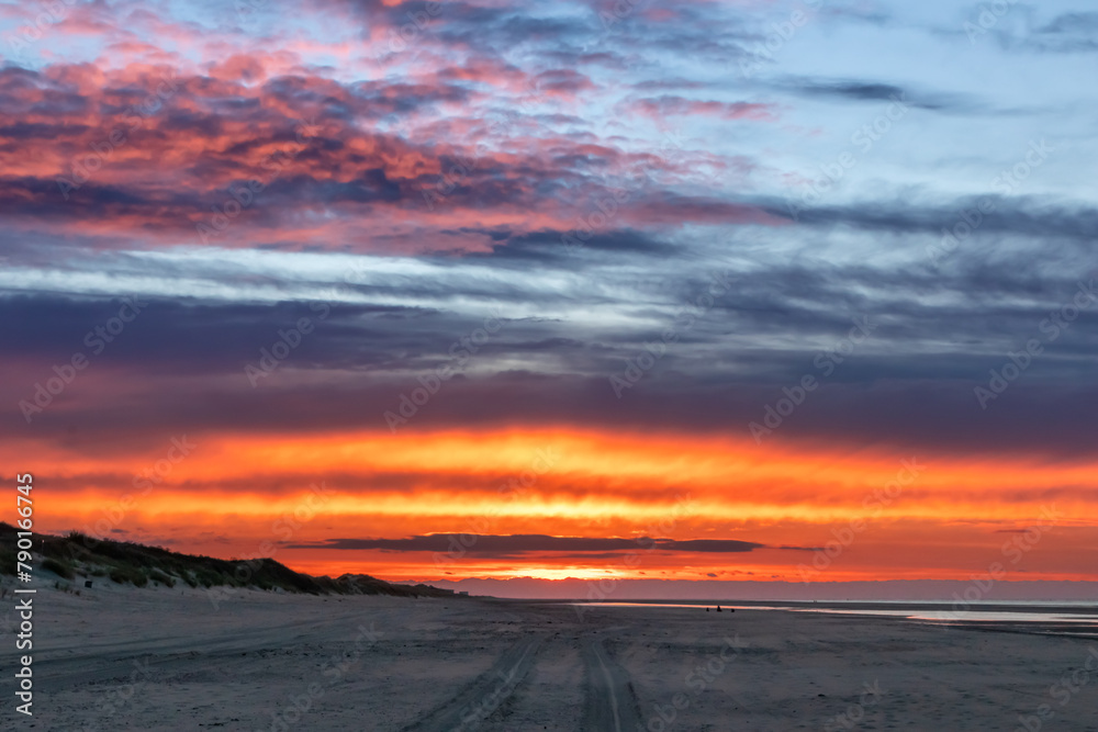 Fototapeta premium Beautiful golden hour beach sunset with glowing sun and colorful sky shows vibrant colors as north sea sand dunes and nature reserve at the ocean in golden hour sunshine as travel destination agents
