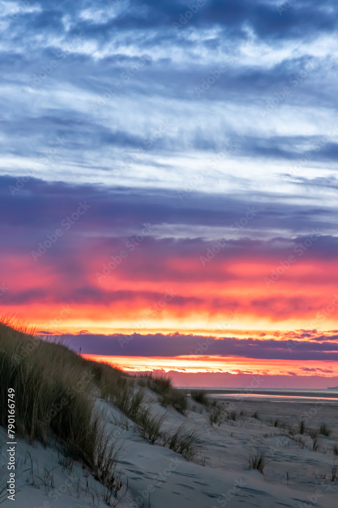 Beautiful golden hour beach sunset with glowing sun and colorful sky shows vibrant colors as north sea sand dunes and nature reserve at the ocean in golden hour sunshine as travel destination agents