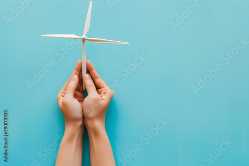 A pair of hands holding a miniature wind farm model, isolated on an alternative energy sky blue background, for World Environment Day photo