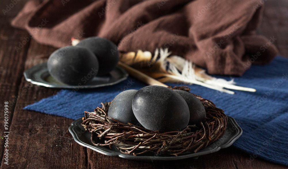 Wine painted eggs in a nest, bird feathers, drapery on a wooden background. Easter concept.