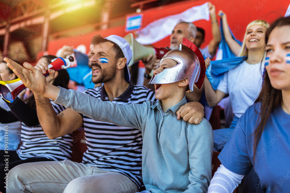Sport fans cheering at the game on stadium. Wearing blue and white colors to support their team. Celebrating with flags and scarfs.