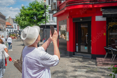 elderly stylish female tourist taking photographs of a unique red house on street,active lifestyle and use of technogy photo