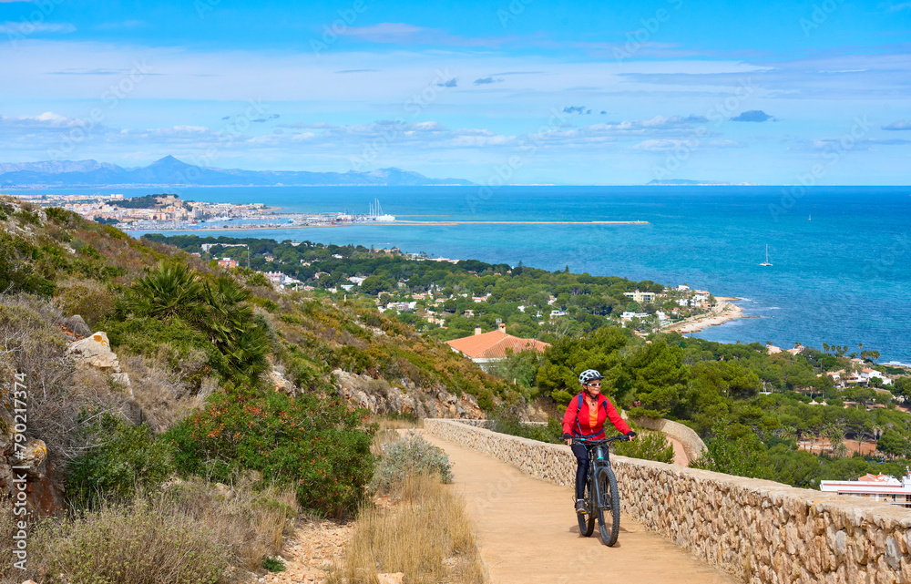 activ senior woman riding her electric mountain bike on the cliffs above the city of Denia, Costa Blanca, Spain, Europe