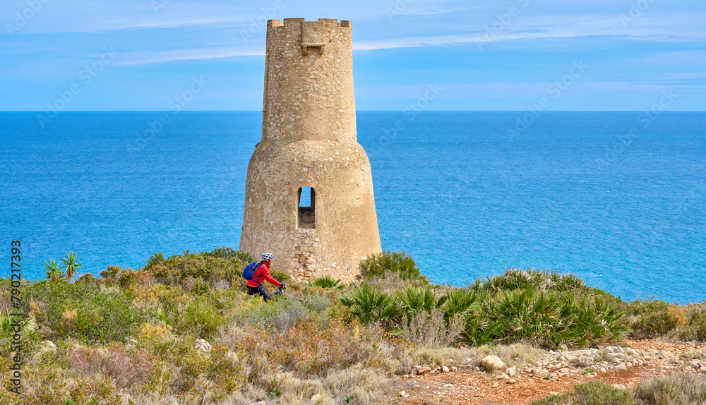 activ senior woman riding her electric mmountain bike at Torre del Gerro on the cliffs above the city of Denia, Costa Blanca, Spain, Europe activ senior woman riding her electric mmountain bike at Torre del Gerro on the cliffs above the city of Denia, Costa Blanca, Spain, Europe