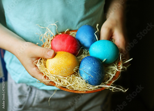 The child holds a basket with painted eggs.