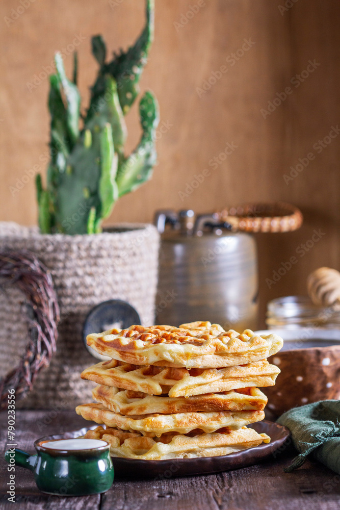 Belgian waffles served with honey, cream and sai on a wooden background. Rustic style.