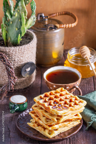Belgian waffles served with honey, cream and sai on a wooden background. Rustic style.