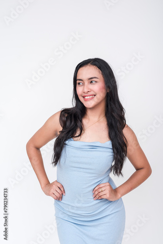 Portrait of a beautiful young woman in a chic baby blue dress standing against a white backdrop. Anticipating and looking at someone to the left.