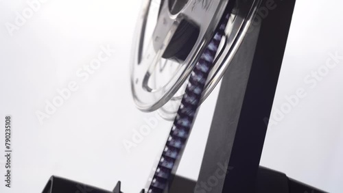 close up of a film projector reel spool turning with a super 8 mm film strip running shaking changing frames detail shot isolated on white background bright light shining through home studio side view