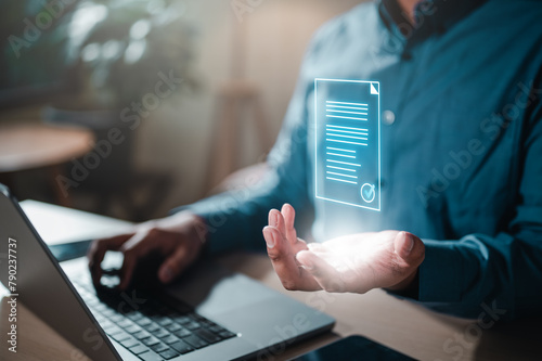 document, file, future, job, management, marketing, occupation, paperwork, strategy, information. A man is holding a piece of paper in front of a laptop. Concept of a document being created or edited.