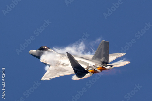 Side view of a F-22 Raptor in a high G maneuver, with afterburners on and condensation clouds at the wing roots