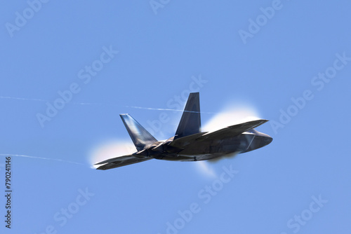 Tail view of a a F-22 Raptor at very high speed, with condensation clouds around the plane