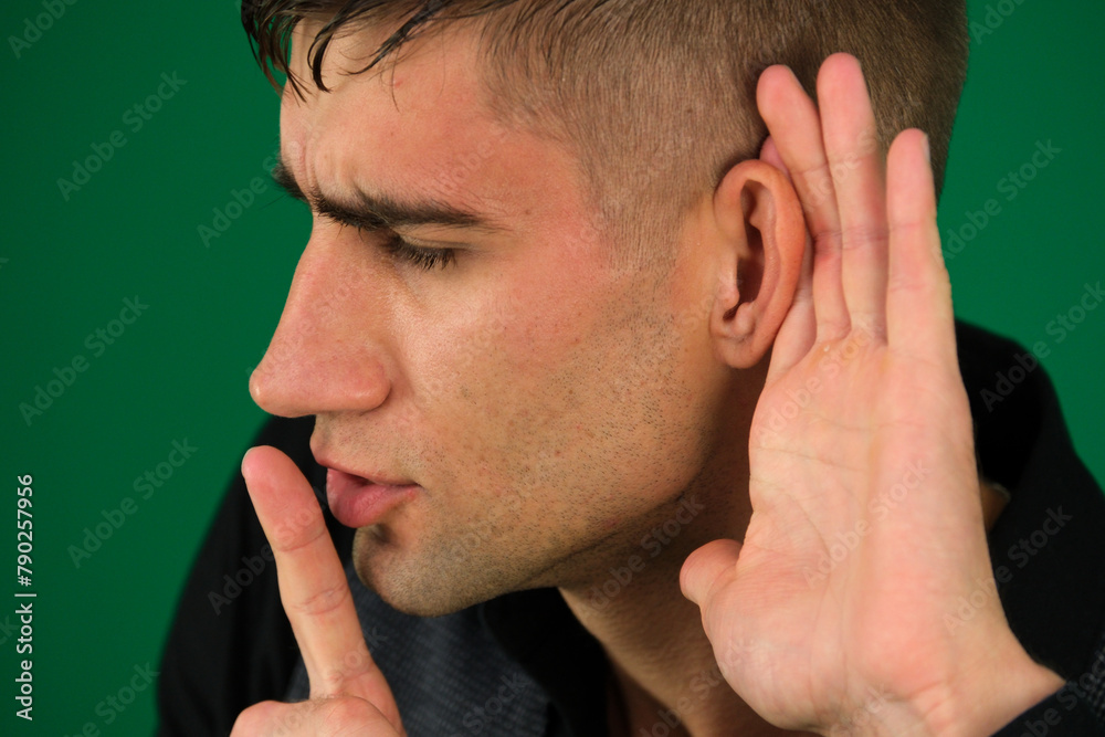Fototapeta premium emotions of a handsome man guy on a green background chromakey close-up dark hair young man. Overhears a man, tries to listen.