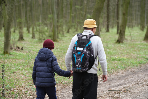 Close up active senior and his grandson walking the forest path holding hands, turned back. Happy family active outdoor. Active activity in old age