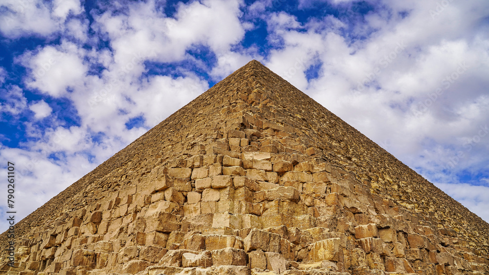 Perfectly symmetrical view of the Great Pyramid of Khufu with its yellow limestone blocks against a cloudy sky on the Giza plateau 