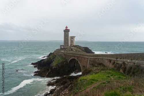 Accessible par un pont qui le relie à son îlot rocheux, le phare du Petit Minou se dresse tel un gardien solitaire au milieu des eaux tumultueuses de la Mer d'Iroise, dans le Finistère, offrant un ref