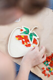 A girl creates strawberries from ceramic mosaics in an open space. 