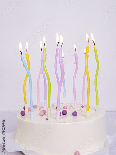Multicolored pastel lighted candles in a white cake , a place for text