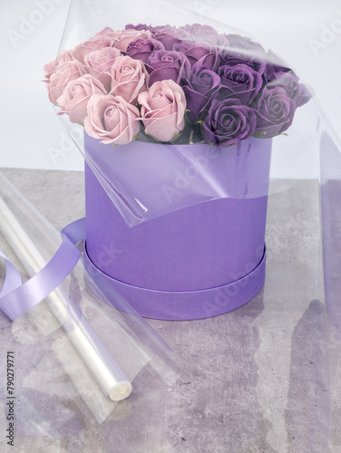 A roll of transparent packaging film and a bouquet of roses in a box on the table