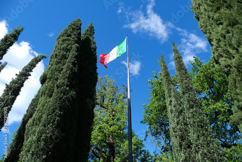 Una bandiera italiana sventola in cima a un pennone, con il cielo blu sullo sfondo.