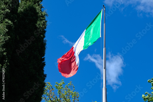 Una bandiera italiana sventola in cima a un pennone, con il cielo blu sullo sfondo.