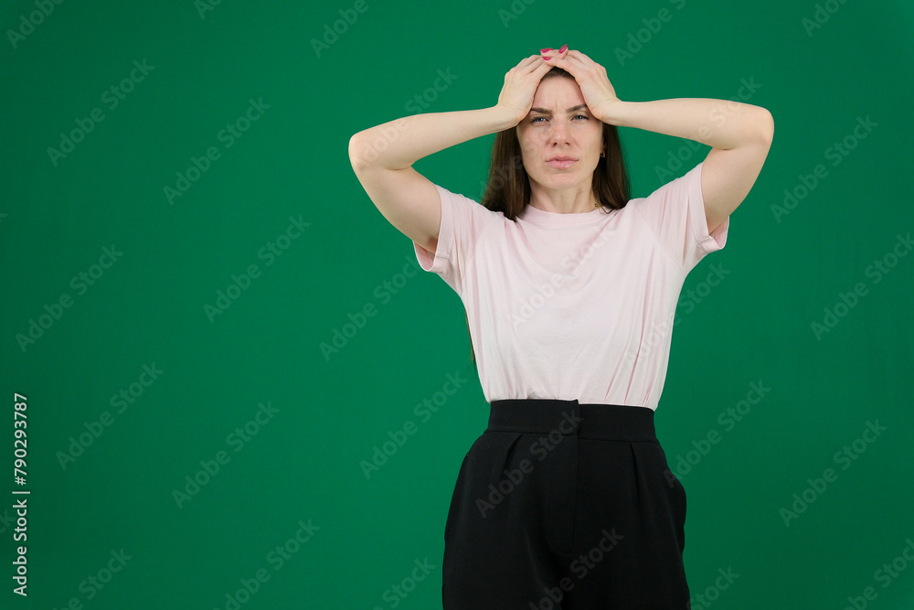 Portrait of concerned tired young woman in green casual clothes looking camera, putting hands on head isolated on bright blue wall background in studio. People lifestyle concept. Portrait of concerned tired young woman in green casual clothes looking camera, putting hands on head isolated on bright blue wall background in studio. People lifestyle concept.