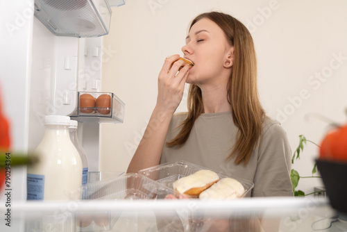 A hungry girl eats a sweet dessert from the fridge. Skinny girl eats stress in the kitchen. The concept of eating disorders