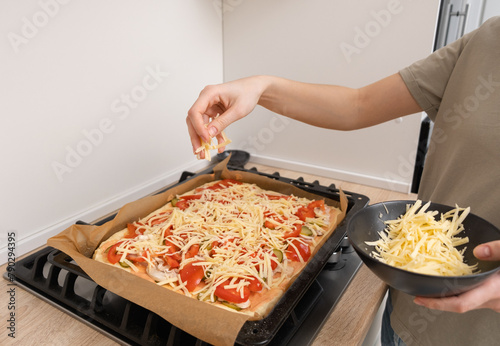 The girl puts the pizza in the oven. A young woman preparing cheese pizza in the kitchen