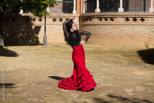 Beautiful woman dancing flamenco in Seville, Spain. She is wearing a red and black gypsy dress and dancing flamenco with a lot of art. In the background a monument with arches and columns.