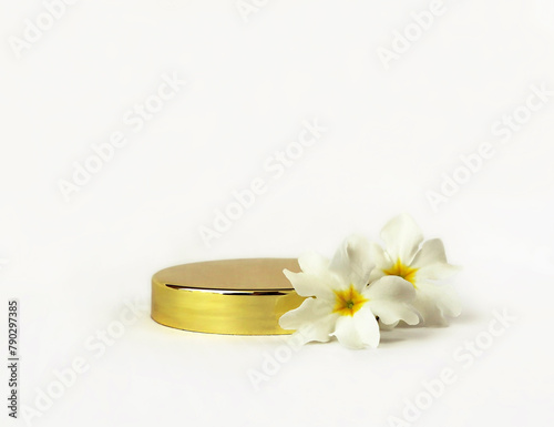 Shiny steel gold round podium with primrose flowers on a white background for luxury beauty. Cosmetic product display backdrop.