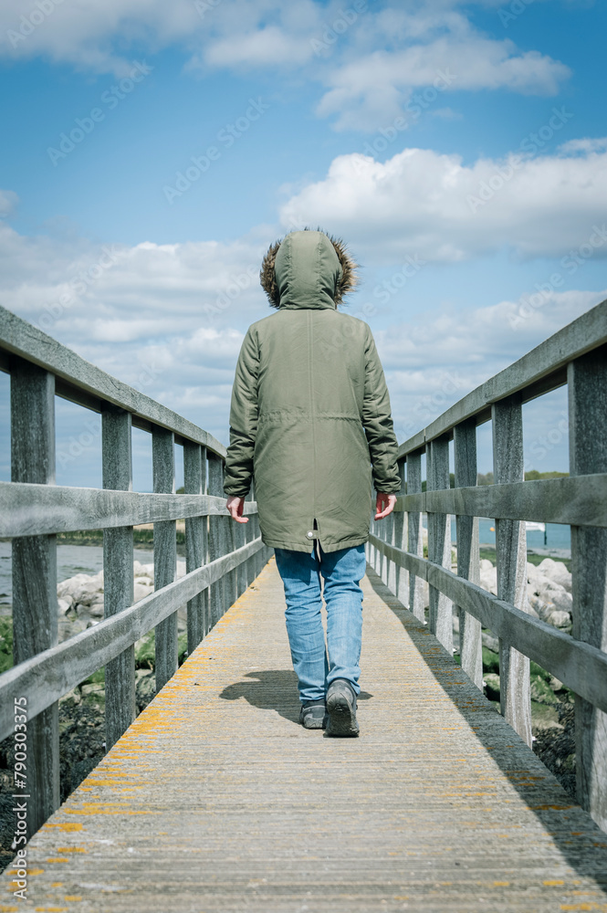 Rear view of a woman wearing a Parka coat walking along a wooden bridge