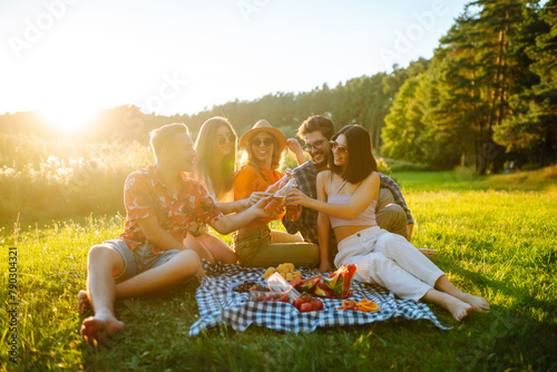 Group of young people having fun while drinking beer at picnic party. Friends enjoy sunny day. Vacation, weekend, friendship or holliday concept.