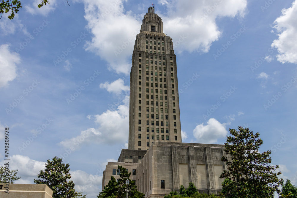 Fototapeta premium The Louisiana State Capitol building with lush green trees, blue sky and clouds in Baton Rouge Louisiana USA