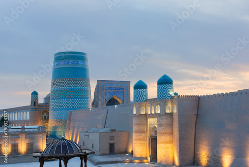Historic architecture of Kalta Minor minaret old at square and Castle gate with illumination at sunset in Itchan Kala inner town of the city of Khiva, Uzbekistan.
