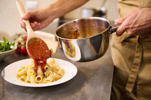 Close up of professional chef plating up pasta before serving it to the customer.