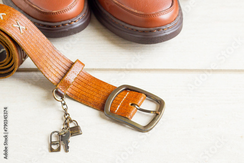 Brown leather belt with men's shoes on wooden surface