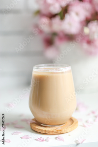 Coffee with milk in a transparent glass without an ear in the sun's rays, a bouquet with Japanese cherry blossoms stands on the back