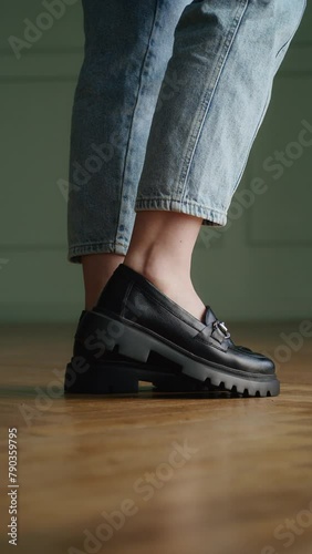 Person wearing chunky black loafers with blue jeans. Close-up side view shot with wooden floor background. Modern fashion and urban streetwear concept for design and advertising.