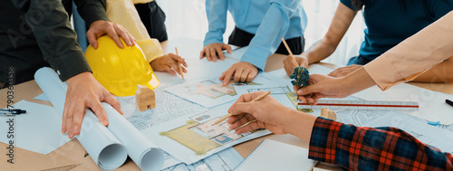 Professional architect cooperate with engineer discussing the use of green design in eco house project on table with blueprint and architectural equipment scatter around. Closeup. Delineation. photo