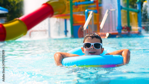 Cute baby boy in white sunglasses swimming with a blue inflatable ring in the clear water of the pool	
