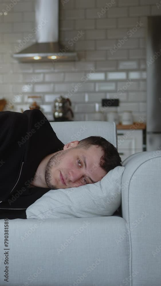 Vertical video. Tired man lie down on the sofa and taking nap with casual clothes. Rest and relaxation after hard day at work making break in living room at home.	