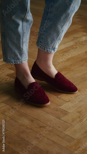 Person wearing burgundy slip-on shoes with rolled-up blue jeans on a herringbone parquet floor. Casual footwear style and comfortable fashion concept for design and advertising.
