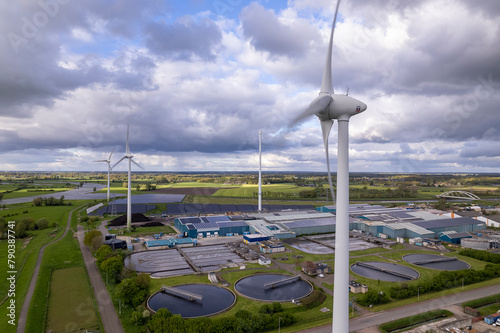 Wind turbines, water treatment and bio energy facility and solar panels in The Netherlands part of sustainable industry in Dutch flat river landscape against blue sky. Aerial circular economy concept.