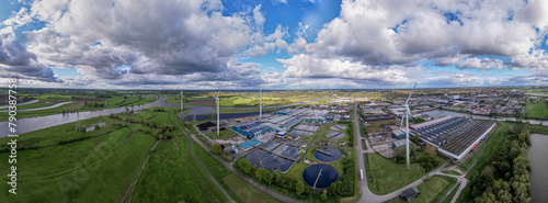 Wind turbines, water treatment and bio energy facility and solar panels in The Netherlands part of sustainable industry in Dutch flat river landscape against blue sky. Aerial circular economy concept.