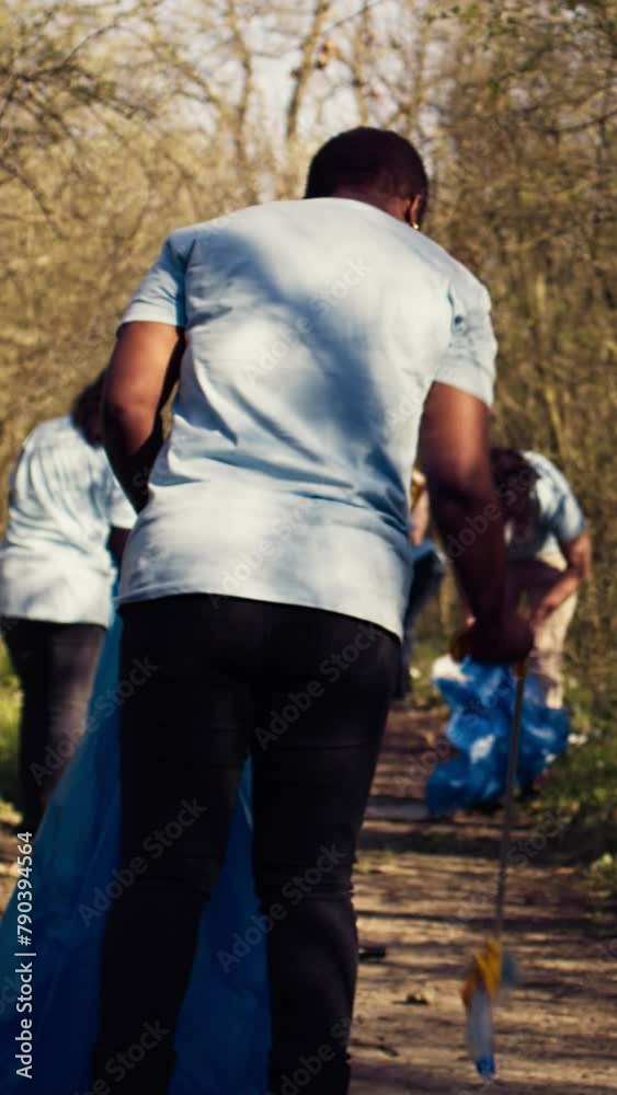 Diverse activists group using claw tools to grab trash and plastic, storing it in garbage disposal bags. People gathering to collect rubbish and recycling for sustainable lifestyle. Camera B. Diverse activists group using claw tools to grab trash and plastic, storing it in garbage disposal bags. People gathering to collect rubbish and recycling for sustainable lifestyle. Camera B.